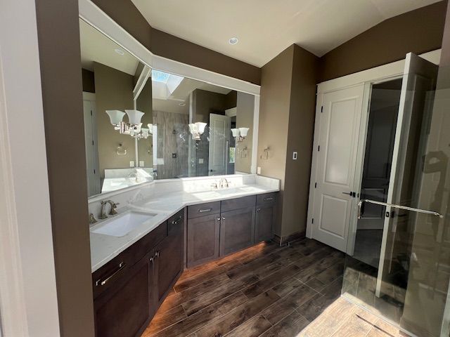 Bathroom with dark brown cabinets, white countertops, large mirror, and wood-look floor.