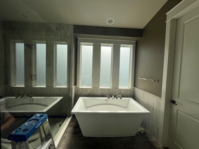 A modern bathroom with a freestanding white tub under a window with frosted glass.