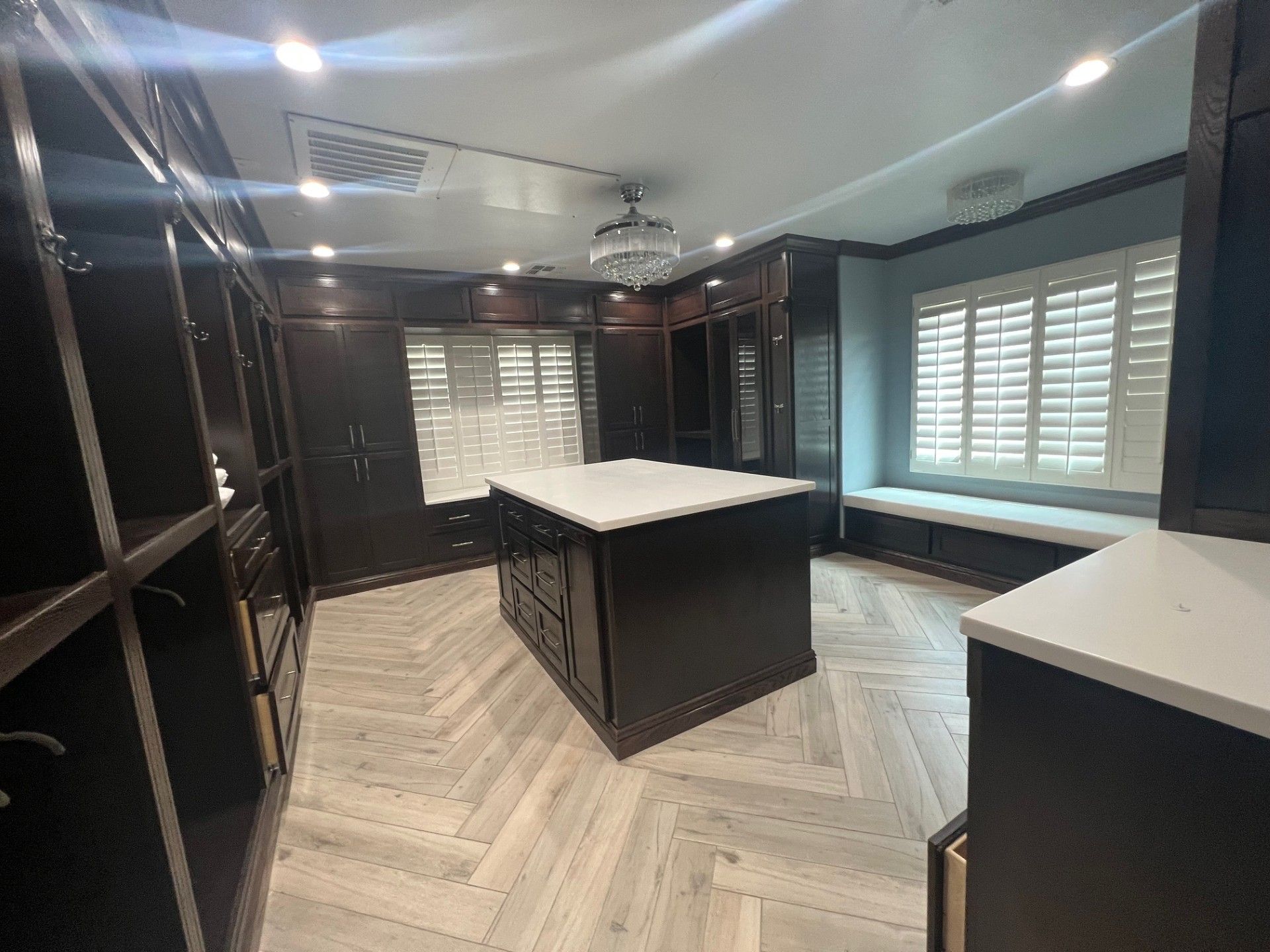 Luxurious walk-in closet with dark wood cabinets, central island, white countertops, window seating, and light wood floors.