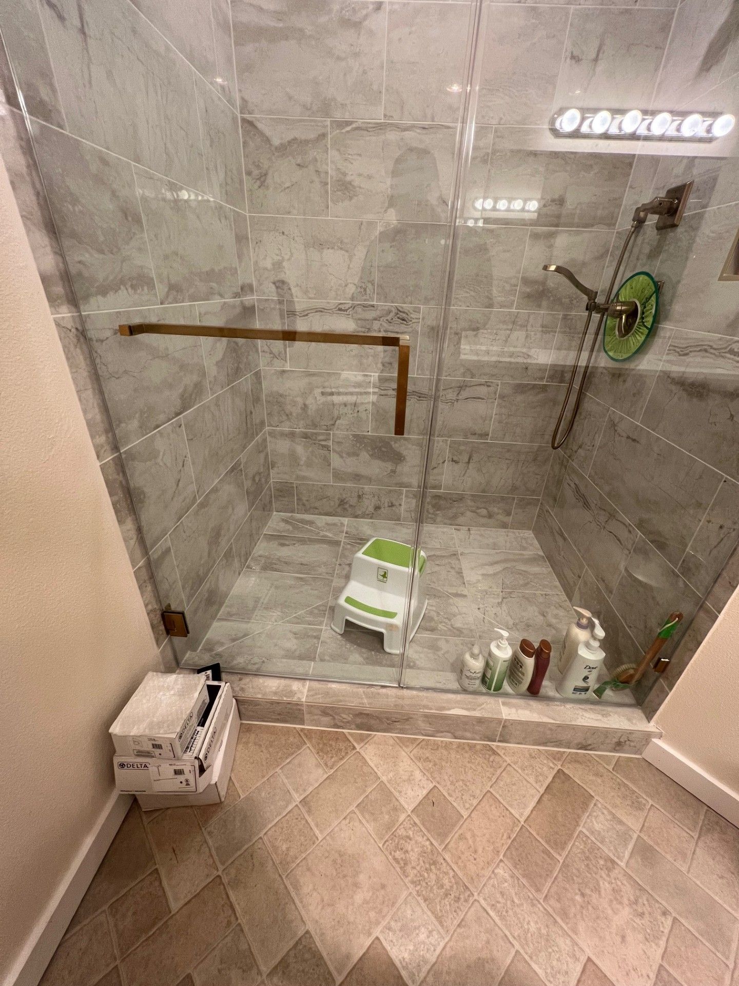 Shower with gray tile walls and glass door; brown and beige floor.