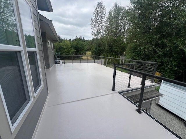 A gray deck with black railings and a bench, overlooking a treeline.