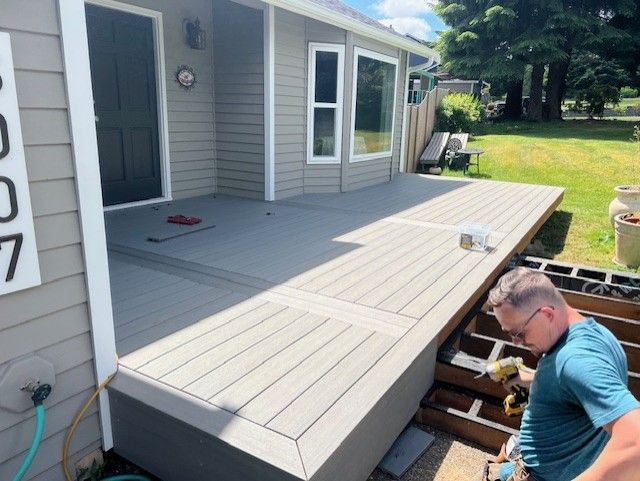 Man building a composite deck on a house. Gray deck and siding. Green grass, sunny day.