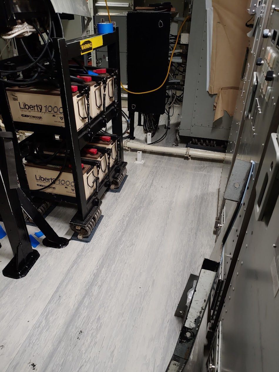 Shelves holding beige batteries next to a metal panel in an industrial setting.