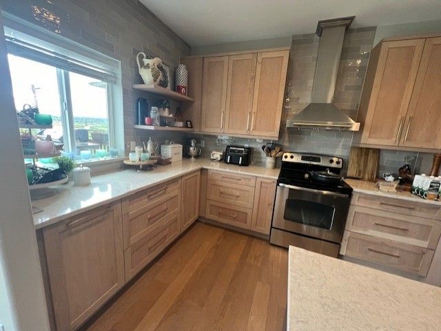 Kitchen with light wood cabinets, stainless steel appliances, and a window overlooking greenery.