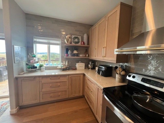 Kitchen with light wood cabinets, countertop, and a stainless steel range with a window overlooking a view.