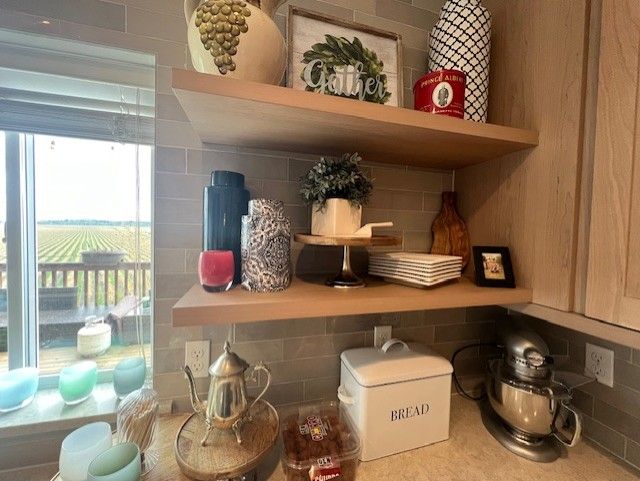 Kitchen shelves with decor: vases, art, plates, and a breadbox. Window with vineyard view.