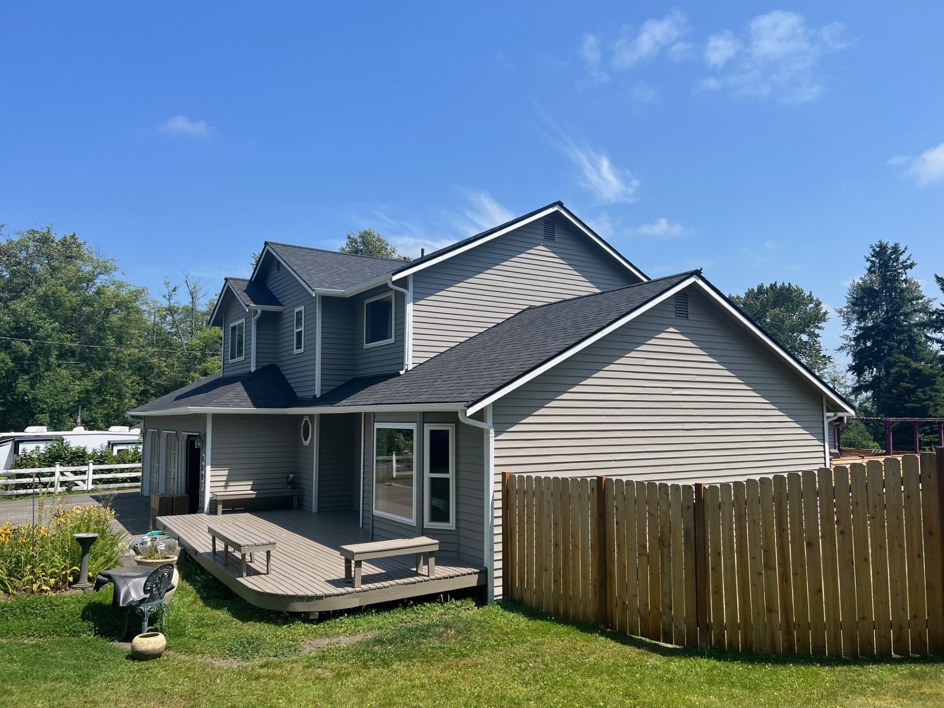 Two-story gray house with a wooden deck, wooden fence, and blue sky.