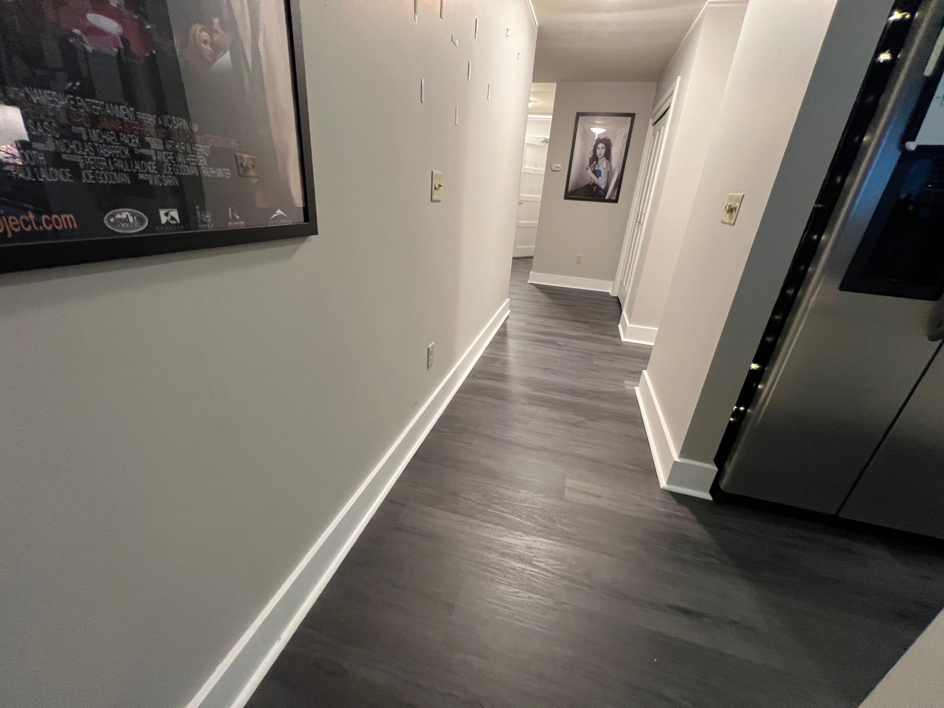 Dark hallway with gray walls, dark wood floors, and artwork.
