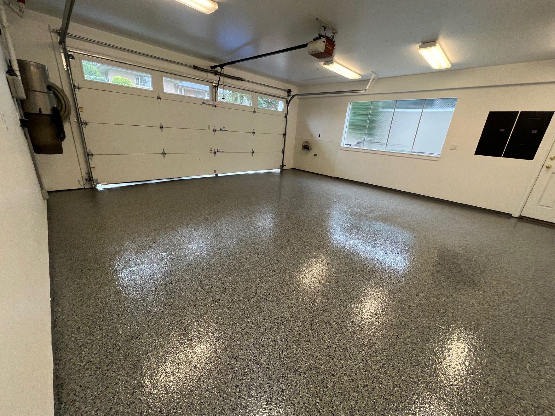 An empty garage with a glossy gray epoxy floor, a closed white garage door, and a small window.