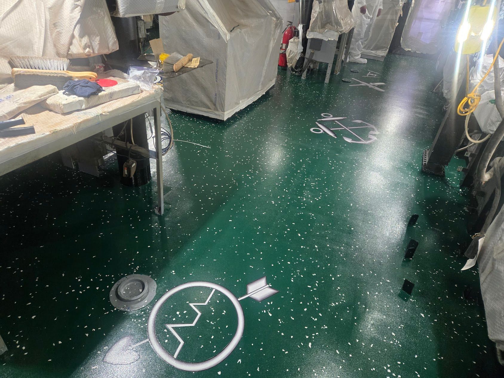 Green floor with white specks, various equipment in a facility, white markings, a table.