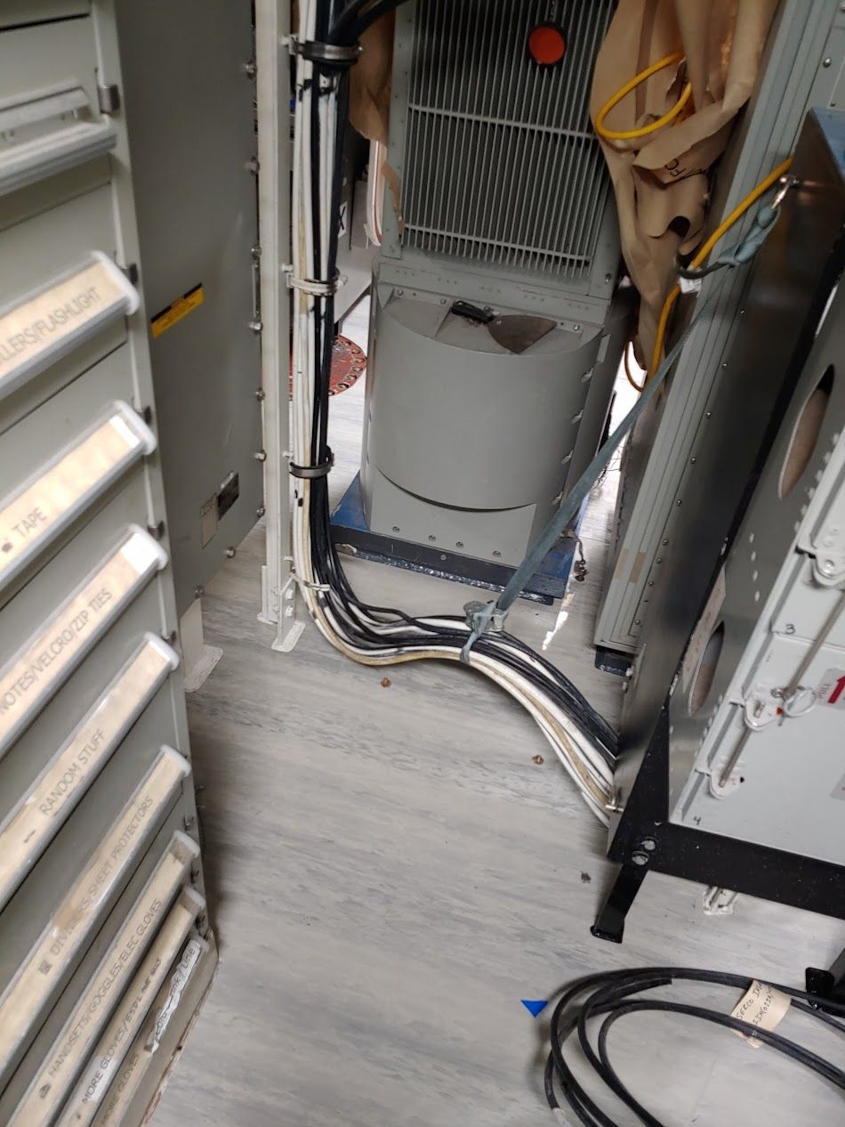 Inside a utility room, bundles of cables are routed along the floor near a metal box.