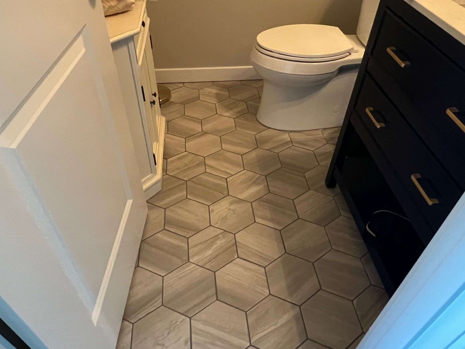 Bathroom with hexagon-patterned floor tile, a white toilet, and dark blue vanity.