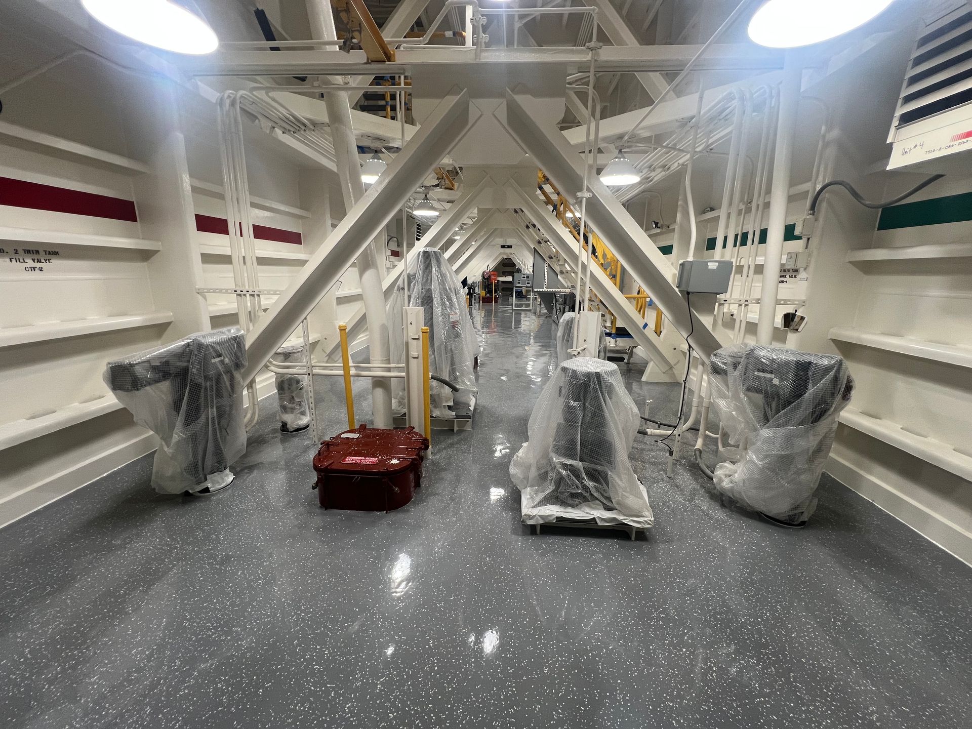 Interior view of a white structure with gray flooring and equipment covered in plastic; overhead lighting.