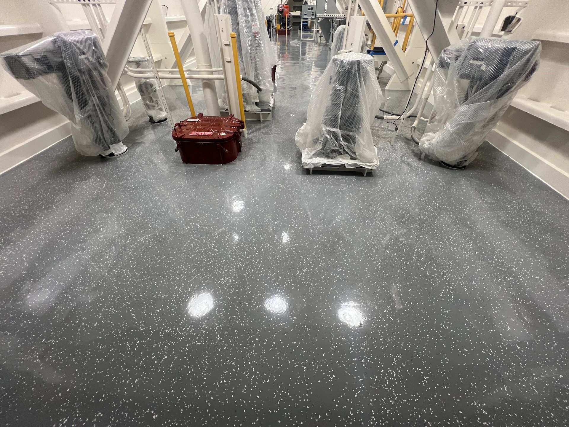 Gray flecked floor in a bright room with covered equipment, red toolbox, and white structural supports.