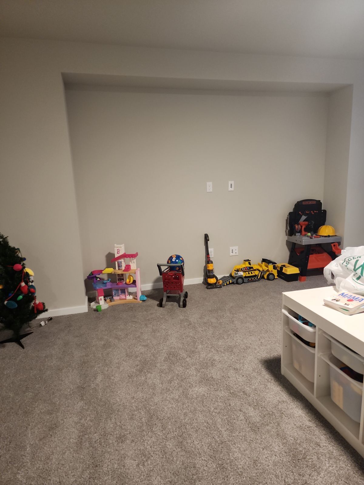 A playroom with toys scattered on gray carpet. Includes dollhouse, trucks, and a tool kit.