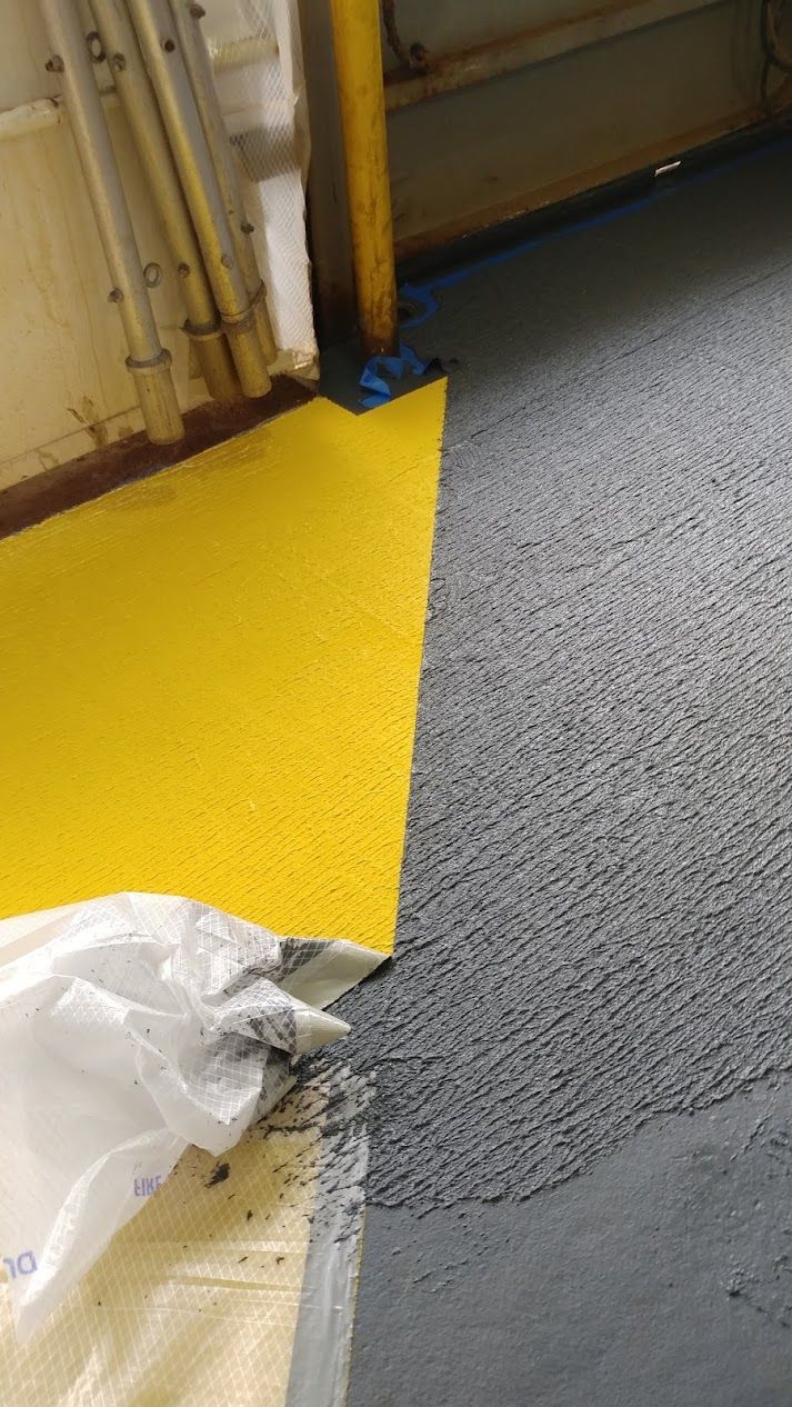 Yellow matting meets gray flooring at a doorway. Debris and a plastic bag are visible.