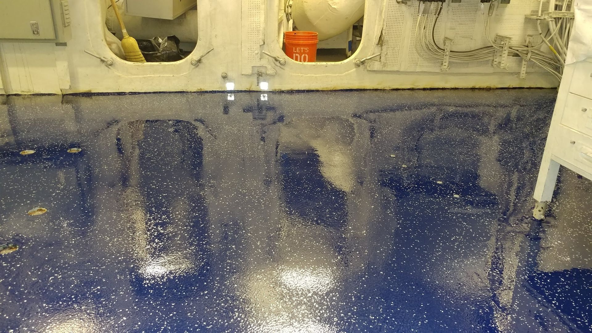 Blue speckled floor inside a white interior with closed doorways and a glimpse of an orange bucket.