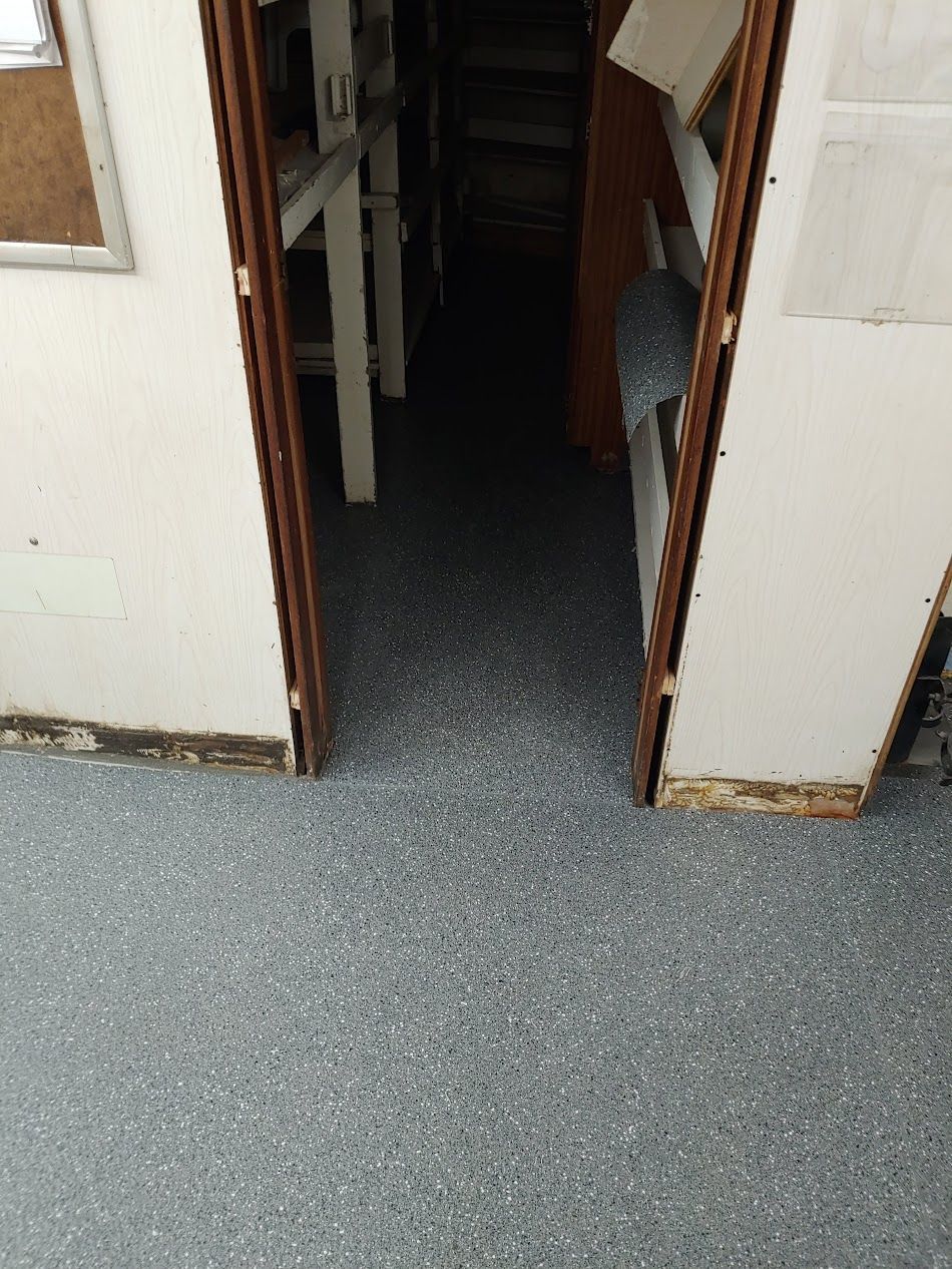 A doorway with worn trim opens into a dark room with speckled gray flooring.