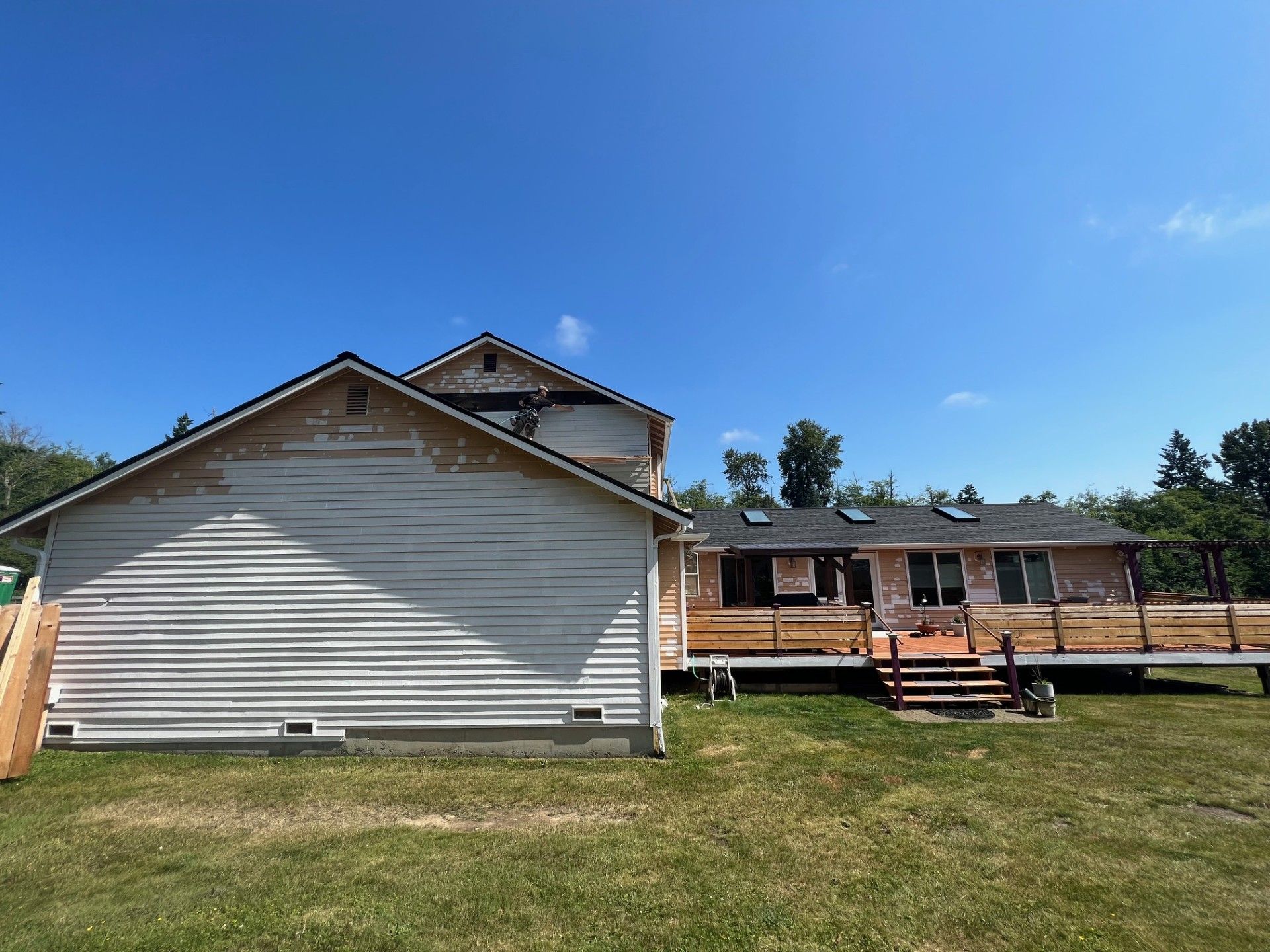 House exterior undergoing renovation; peeling white siding, exposed wood, clear blue sky, sunny day.