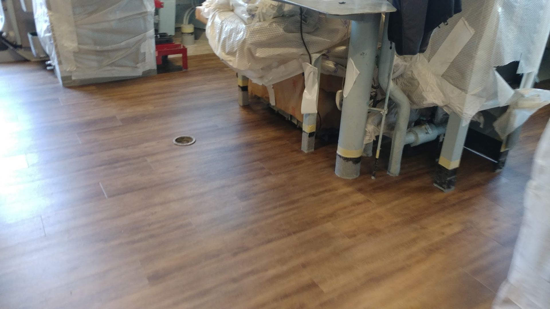 Brown wood-look floor with an object in the center and furniture covered with plastic in the background.