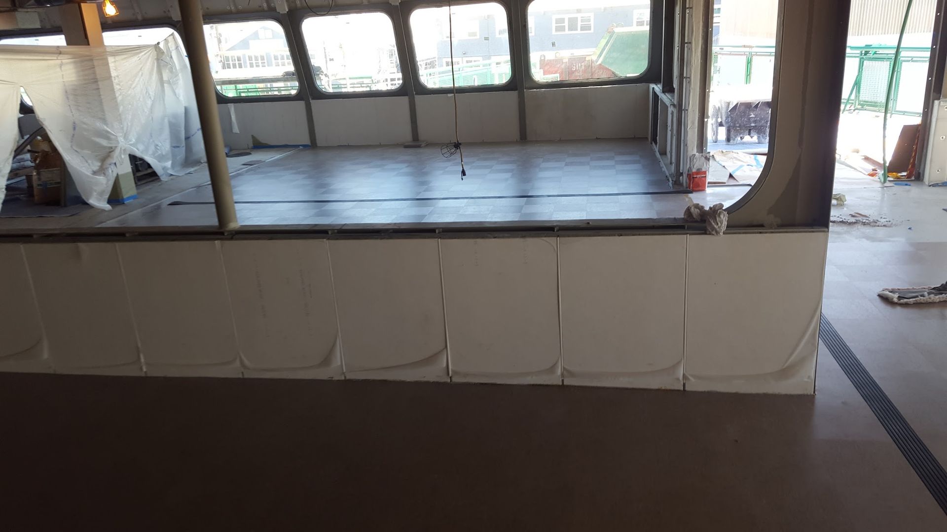 Interior of a boat cabin under renovation; white paneling, grey floor, large windows, and construction materials.