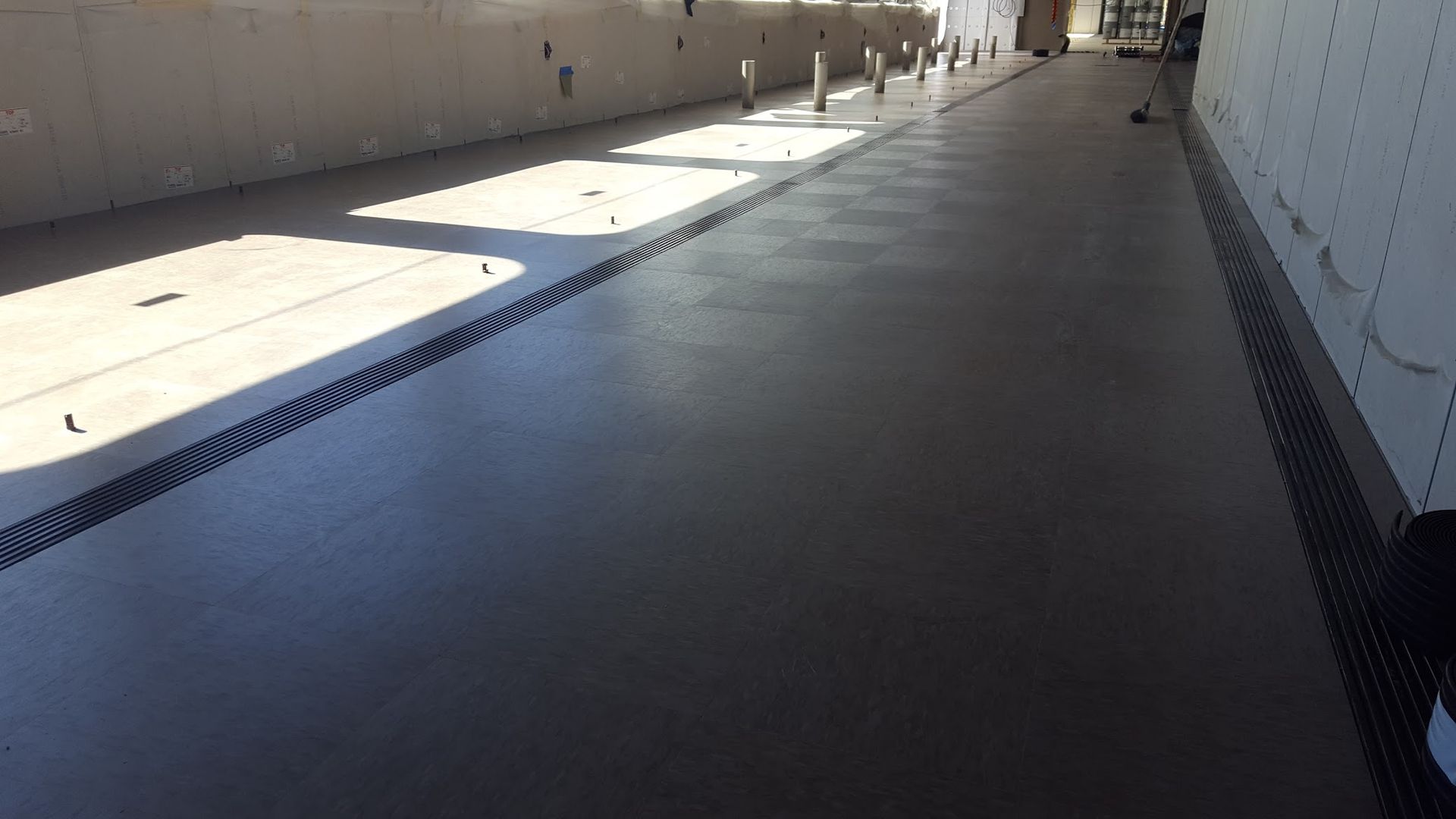 Long, dark-gray concrete floor with linear drainage grates along walls; bright sunlight entering from left.