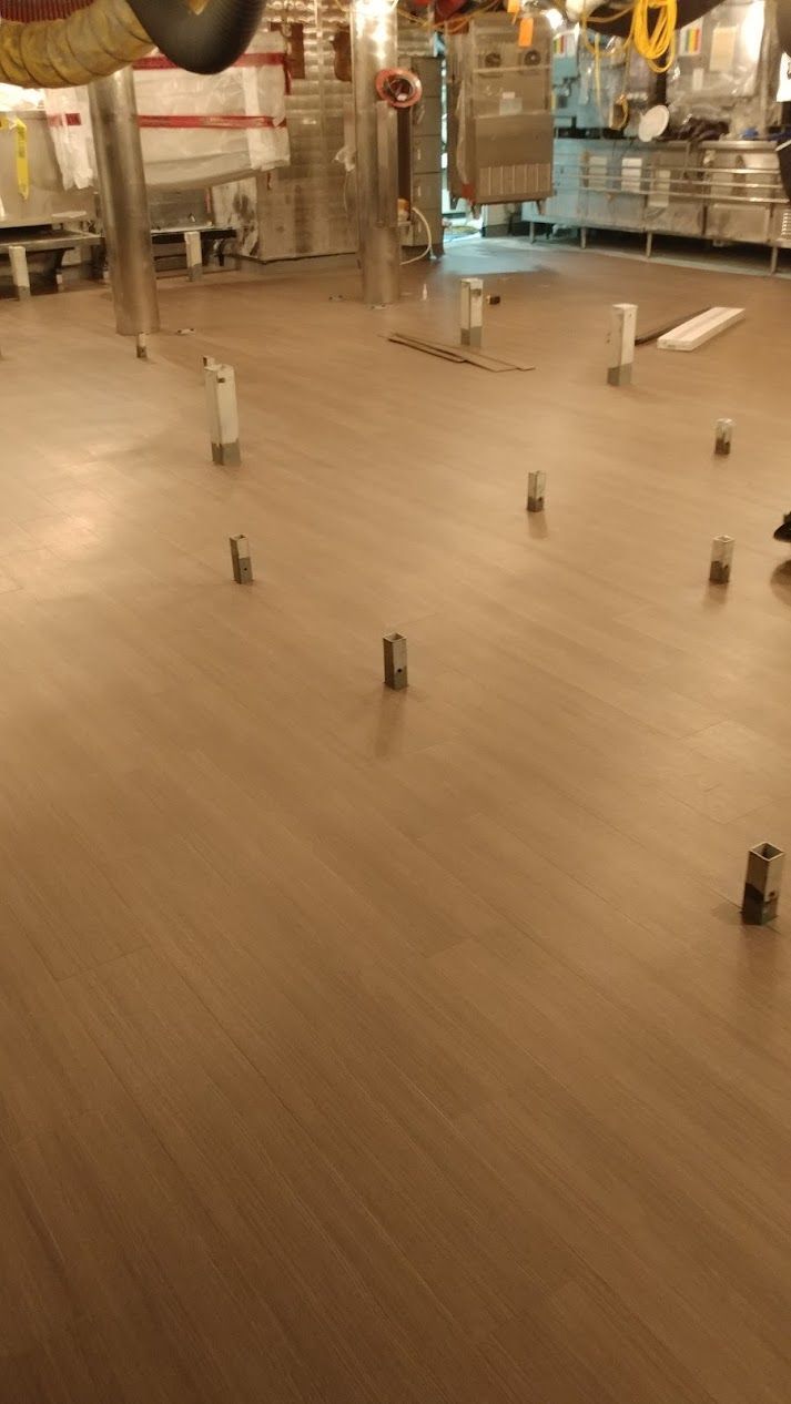 Tan flooring in a factory or industrial setting. Small, metal cylinders are scattered across the floor.