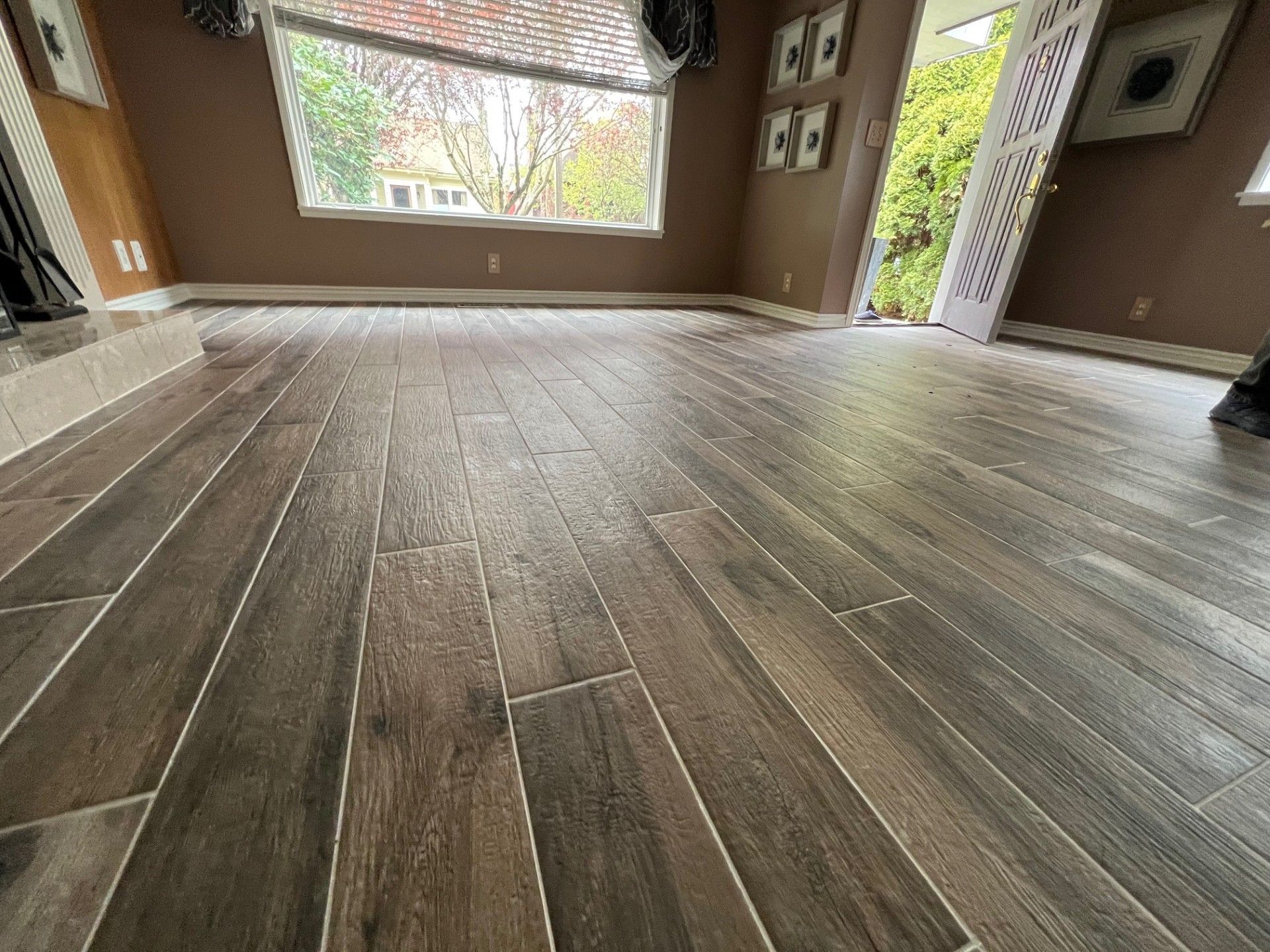 Brown tile floor in a room with a window, open door, and beige walls.
