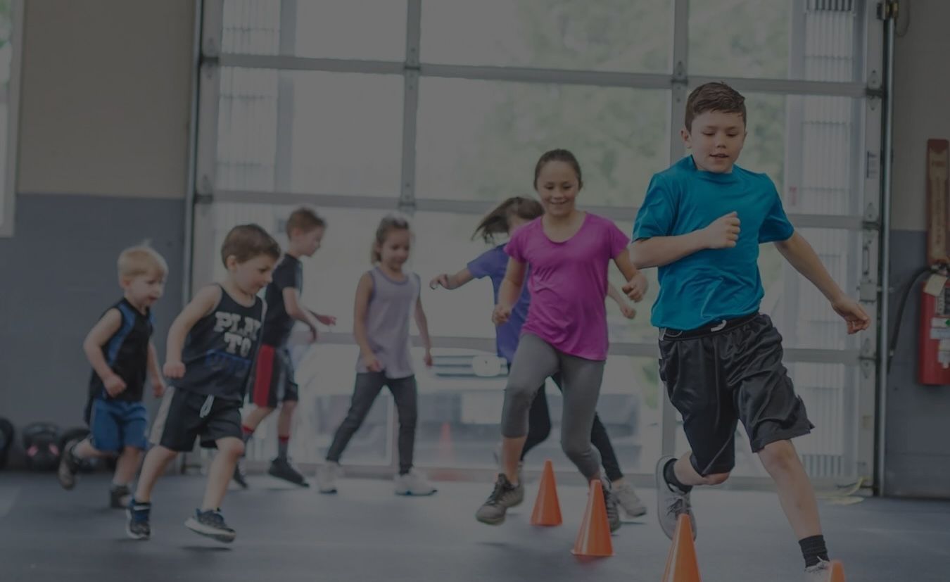 A group of children are running around cones in a gym.
