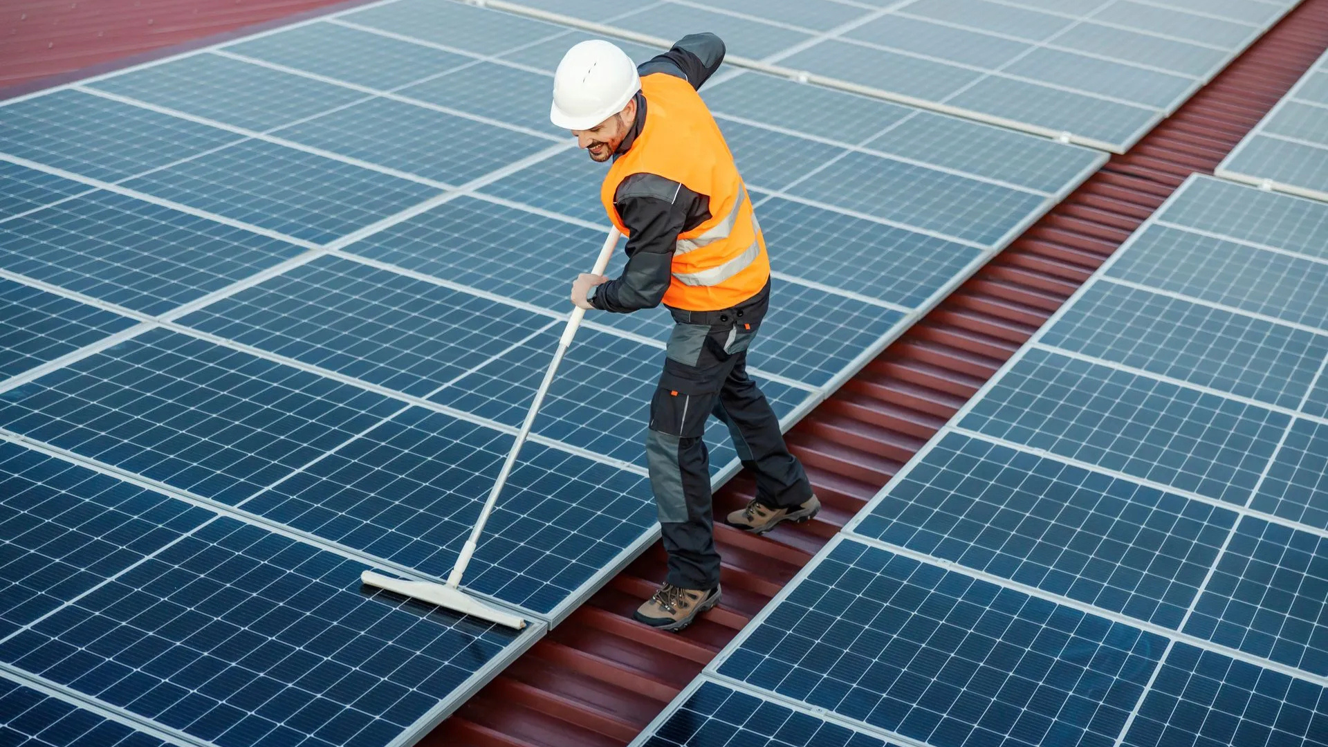 Person in safety gear cleaning solar panels on a rooftop.