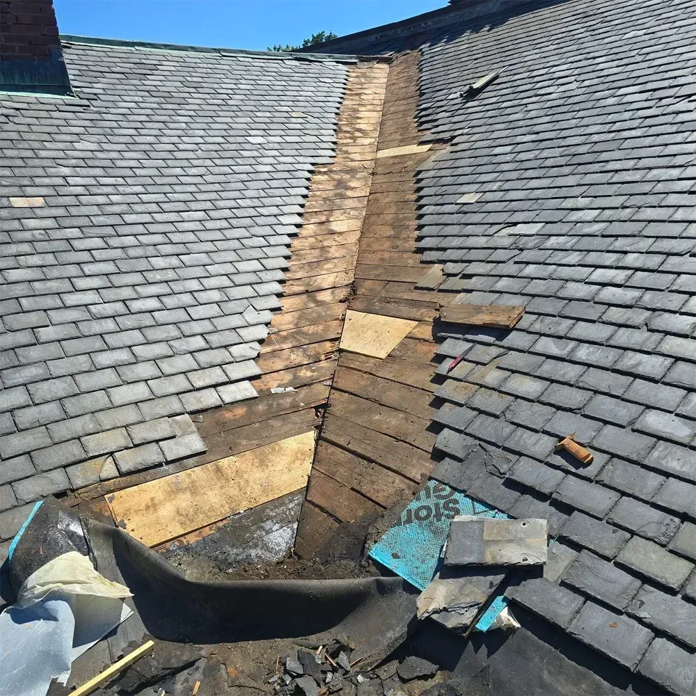 A section of a slate roof undergoing repair, showing exposed wood decking and underlayment in an open valley.