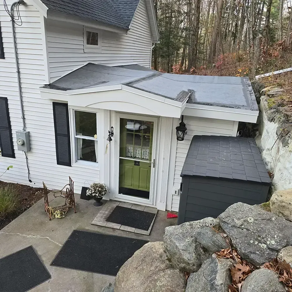 A white house exterior featuring a small, flat-roofed entry porch with a green door, black shuttered windows, and stairs.
