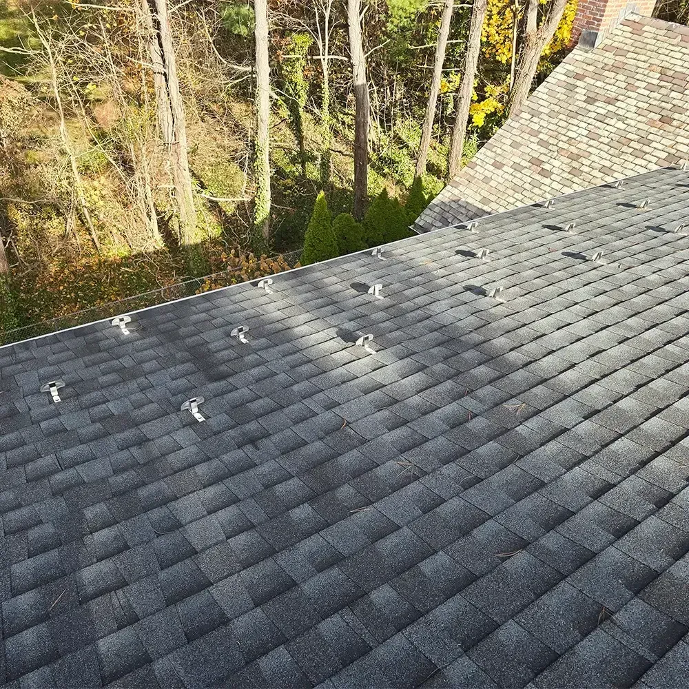 A gray shingled roof with several evenly spaced metal snow guard brackets installed on its surface.