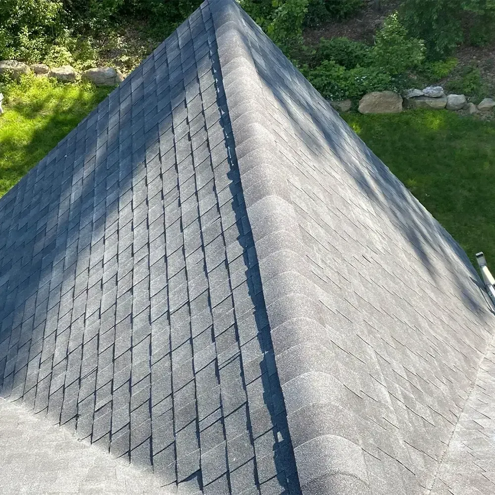 A high-angle view of a gray shingled roof pyramid, with a prominent ridge line and green grass in the background.