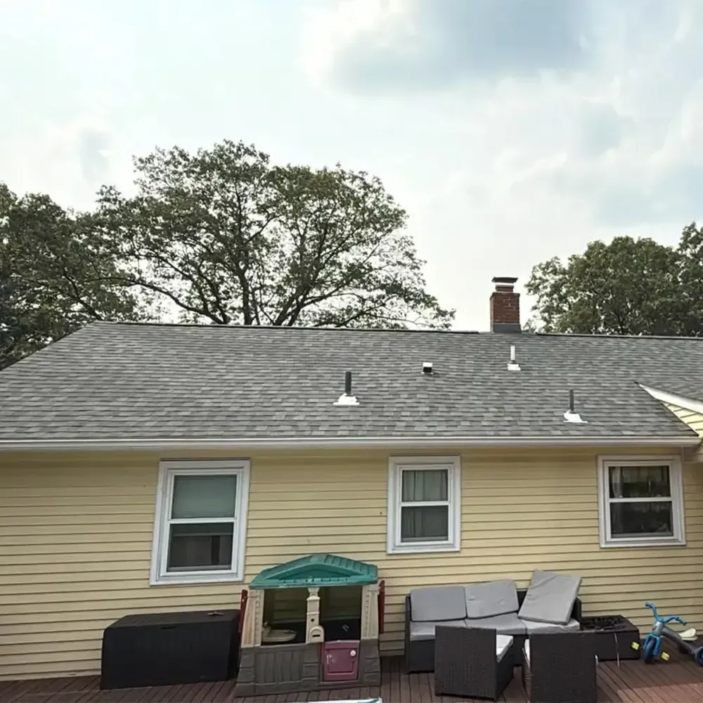 A yellow-sided house with a shingled roof, featuring a deck with a children's playhouse and outdoor seating.