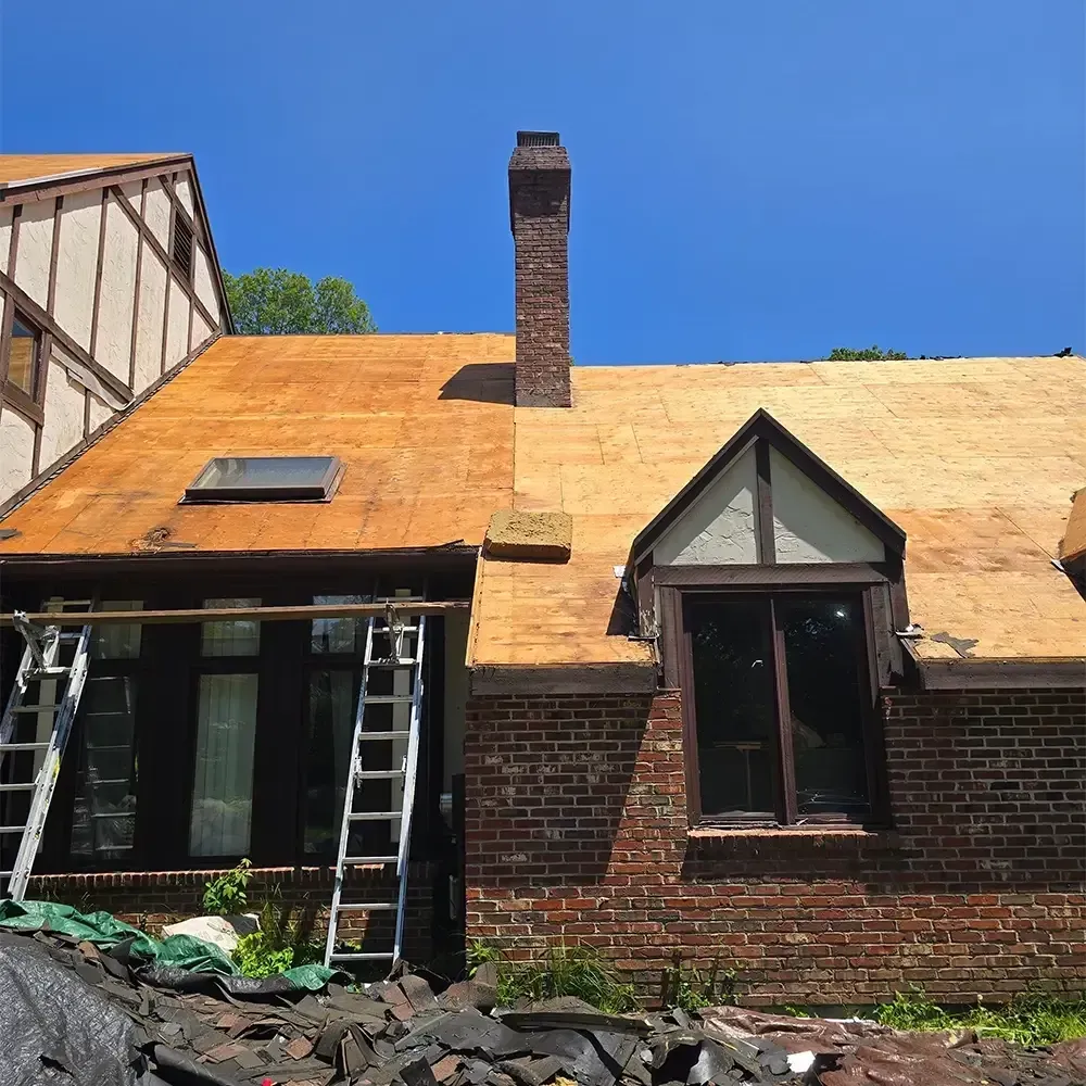 A brick house with a partially re-sheathed roof and a ladder propped against the front, under a clear blue sky.