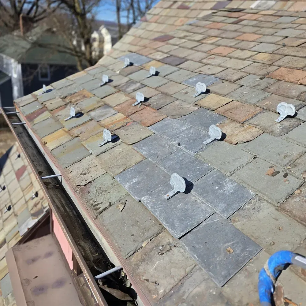A slate roof under repair with several metal slate hooks installed on the tiles.