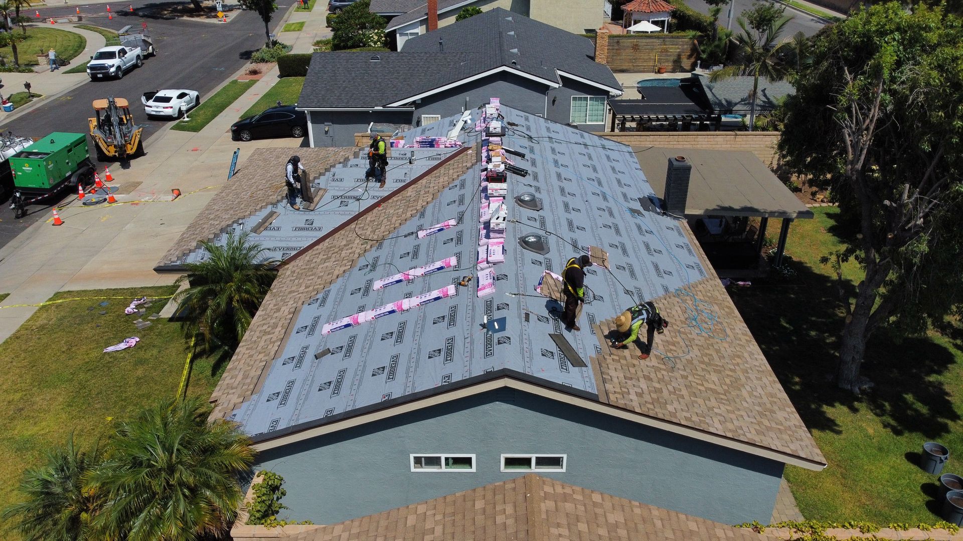 Roofers working on a residential roof, laying down new shingles. Blue house, green truck, sunny day.