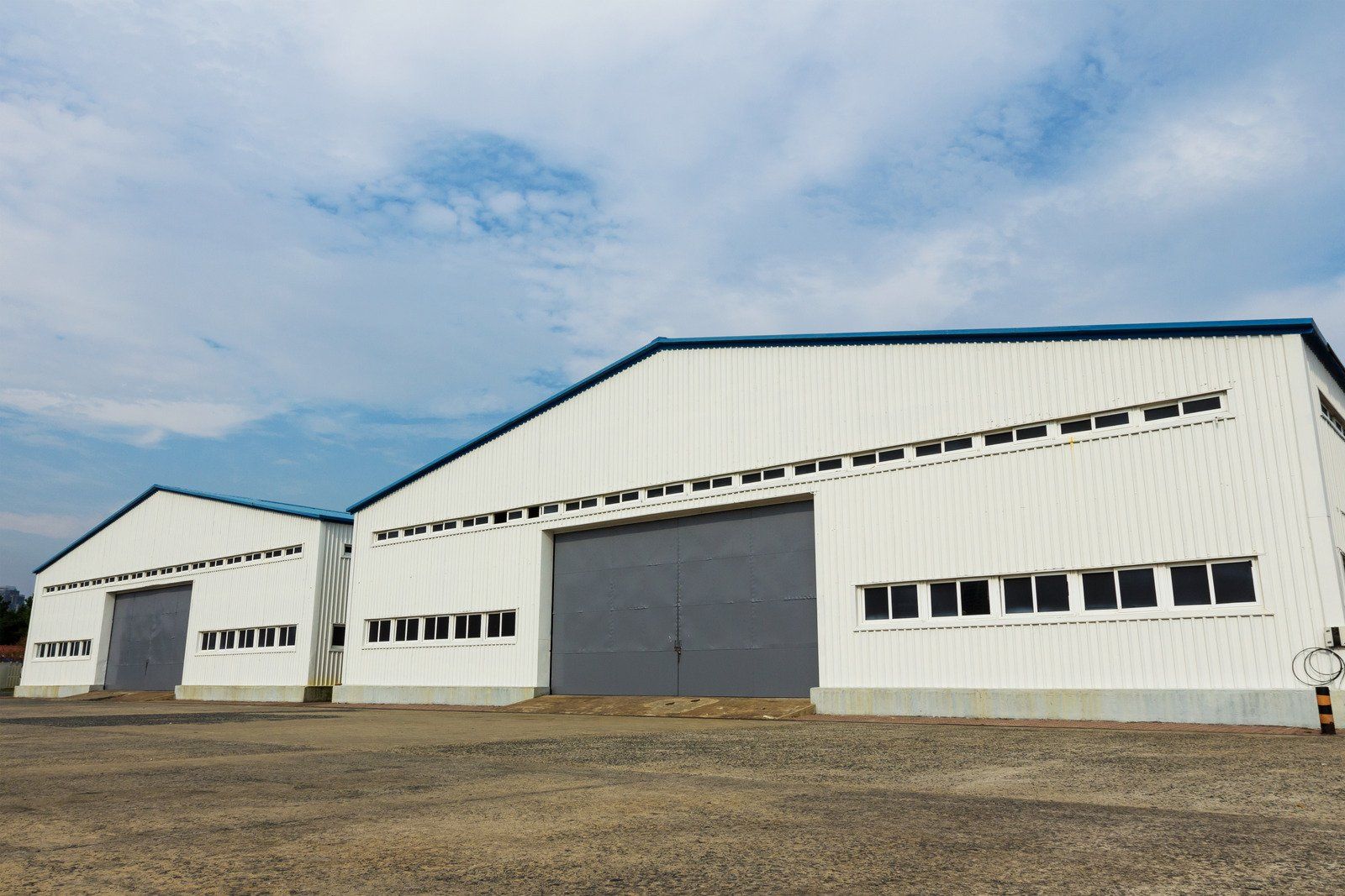 Two white industrial buildings with large gray doors under a cloudy sky.