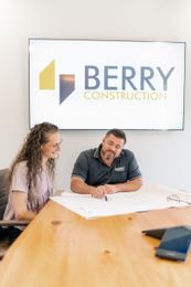 Two construction workers in safety vests and hard hats on a construction site, inspecting materials.
