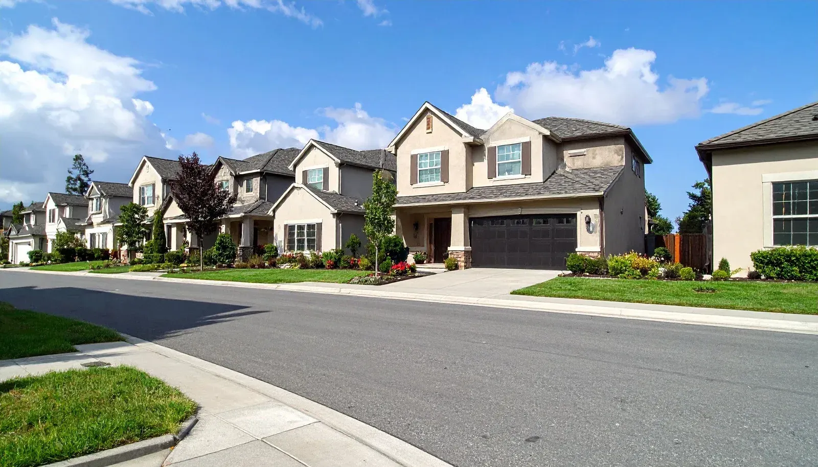 Single-story beige house with gray roof, black driveway, and green lawn under a blue sky.