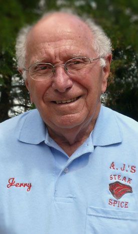 An older man wearing glasses and a blue shirt is smiling for the camera.