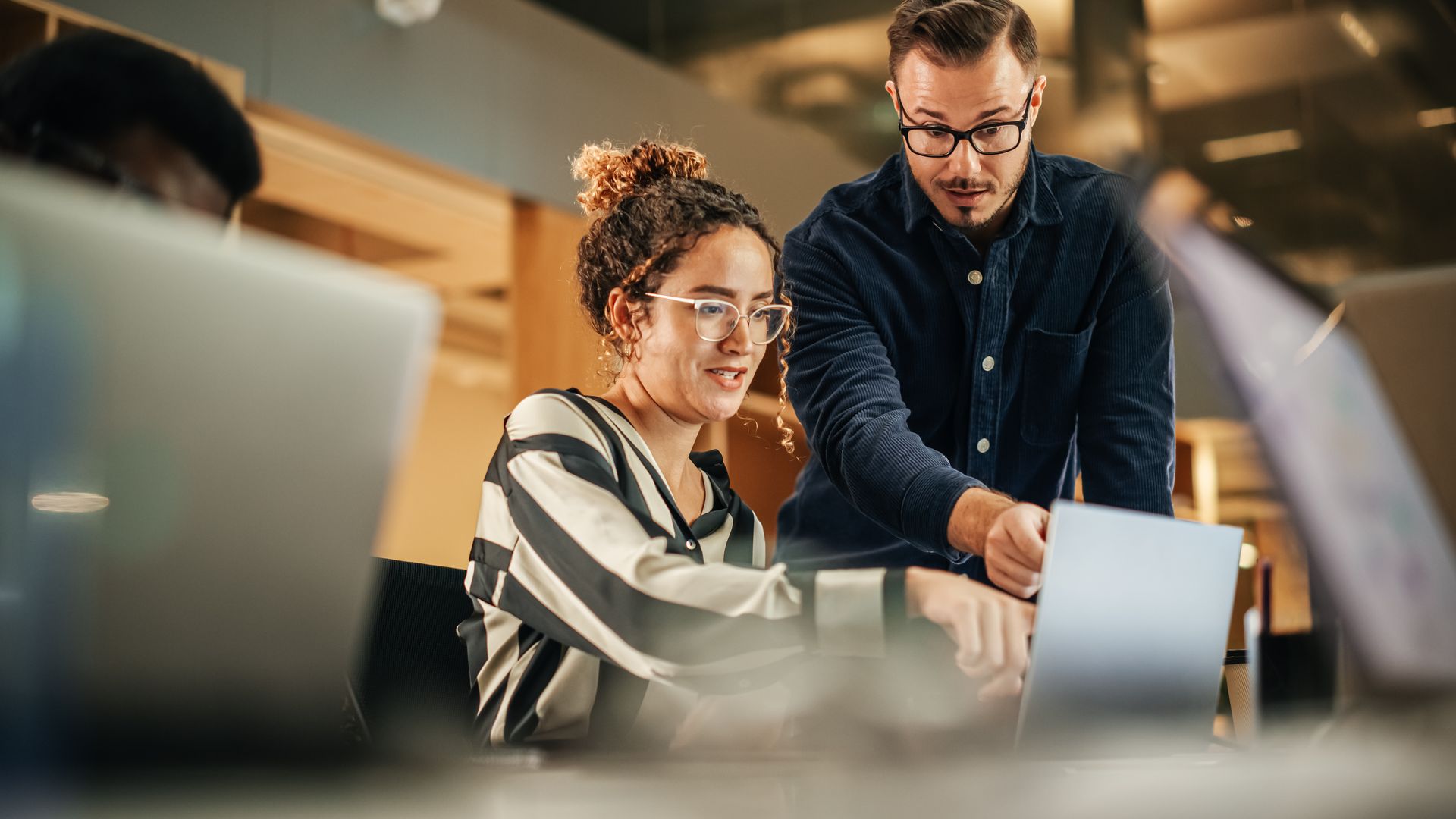 Two people looking at laptop, one pointing at screen in office.