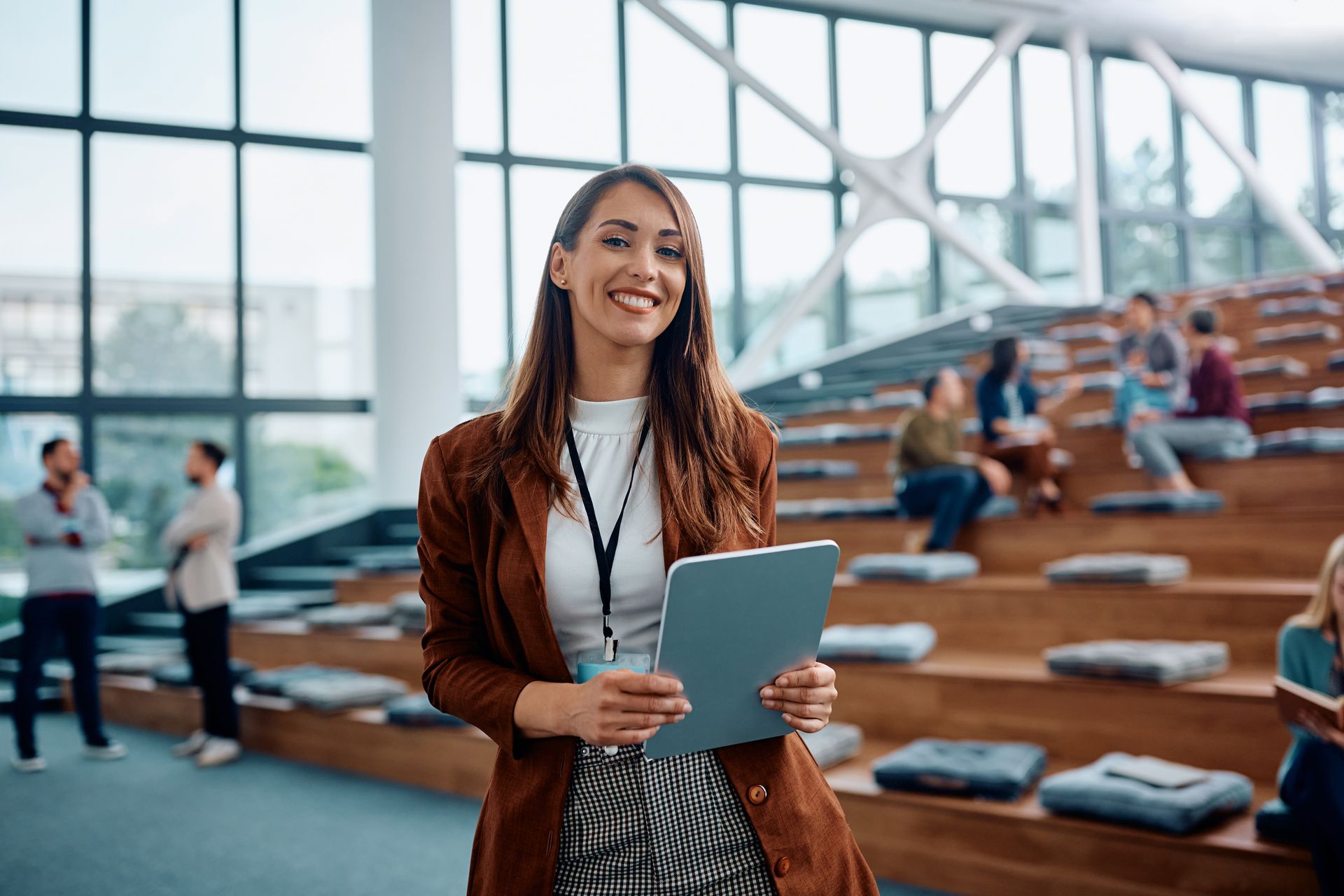 Woman holding tablet smiles in modern building with seating and windows.
