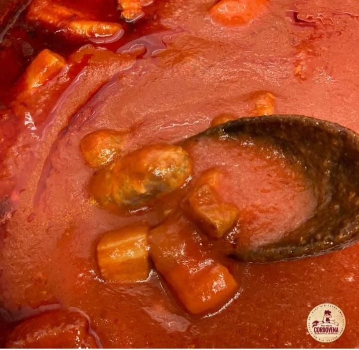 Cibo stufato, salsa rossa, verdure a cubetti, mescolando con un cucchiaio di legno.