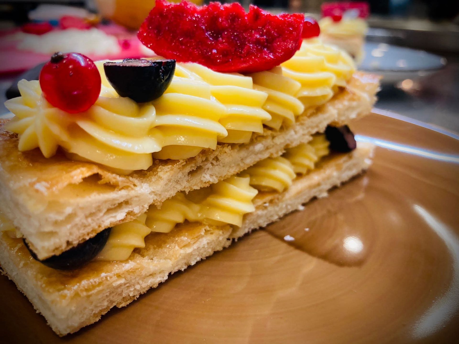 Una pasta sfoglia ripiena di crema e frutti di bosco rossi e neri, servita su un piatto marrone.