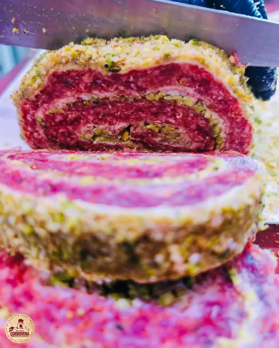 Fette di polpettone tagliato a spirale con una crosta di pistacchi, tagliate con un coltello.