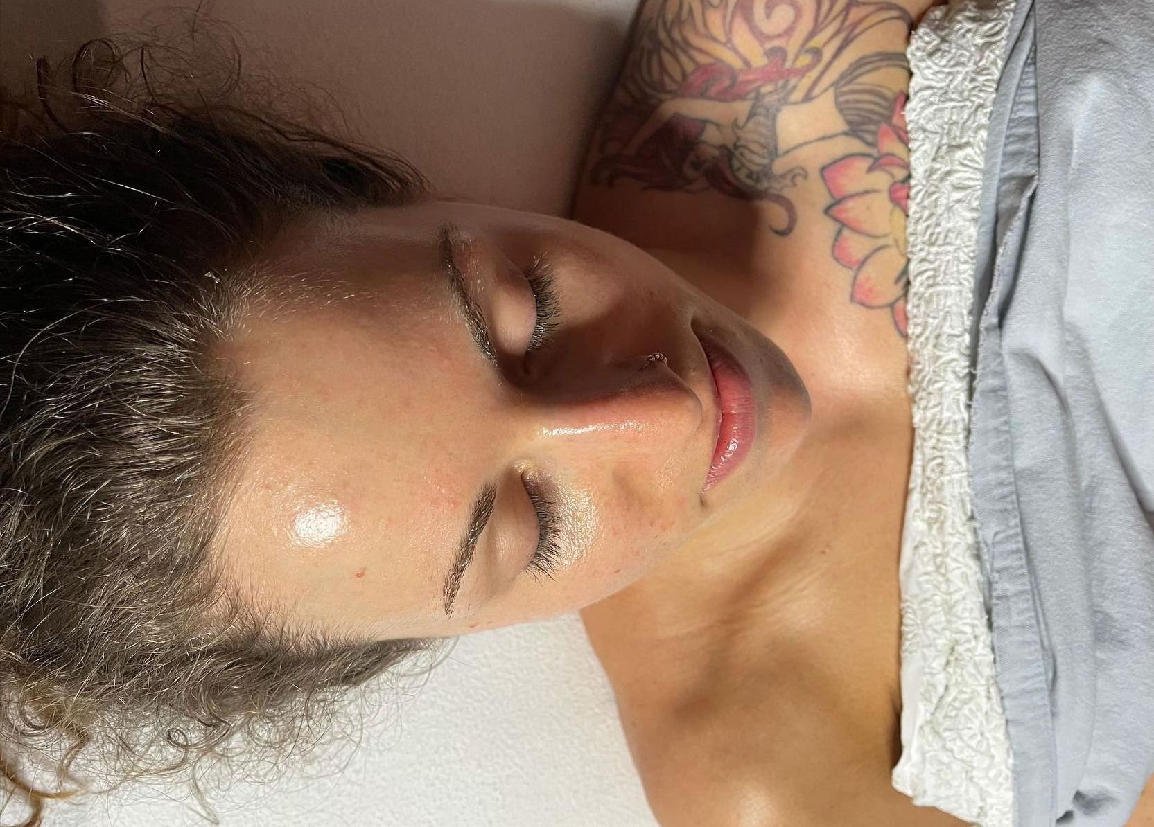 A woman with a tattoo on her arm is laying down with her eyes closed