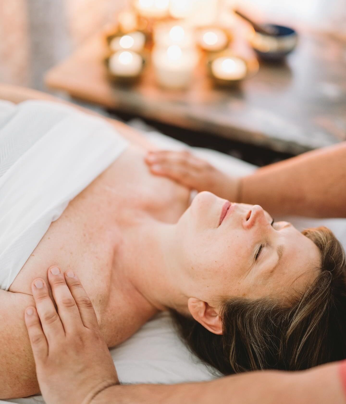 A woman is getting a massage in a spa with candles in the background.