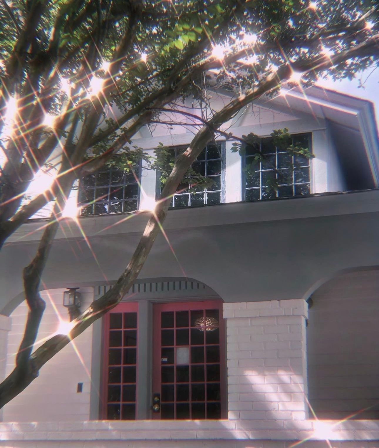 A white house with red doors and a tree in front of it.